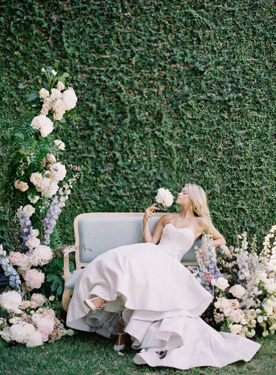 Bride surrounded by large wedding floral installation  on pale blue sofa in front of ivy wall photographed by wedding photographers in Charleston Amy Mulder Photography