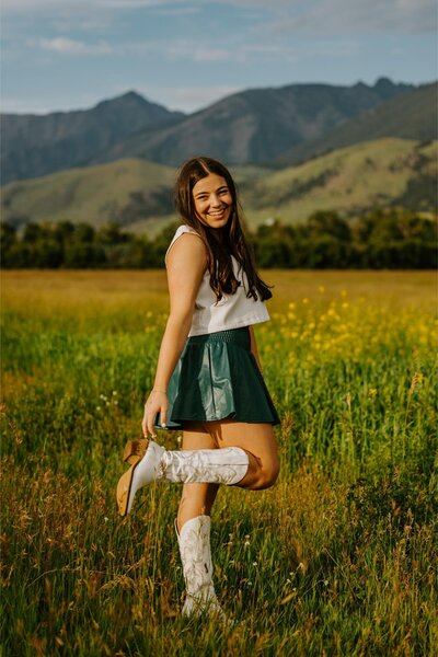 Madeline poses in front of the mountains while wearing white cowboy boots.