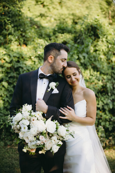 Groom gently places a soft kiss on the bride's head, captured in a tender and intimate moment.