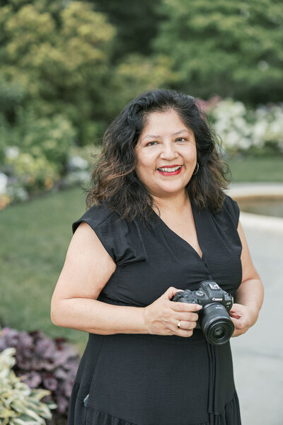 Patricia Parrales, a Brooklyn wedding photographer holding camera in a bautiful Garden.