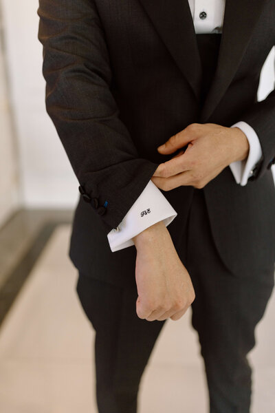 A groom holding his sleeve up to show his custom initial embroidered into his shirt.