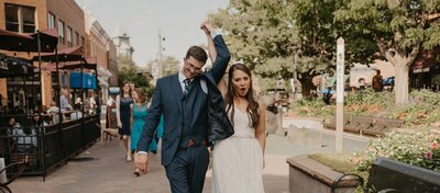 Newlyweds walk hand in hand through a downtown street full of energy and joy, photographed by a Colorado Wedding and Portrait Photographer.