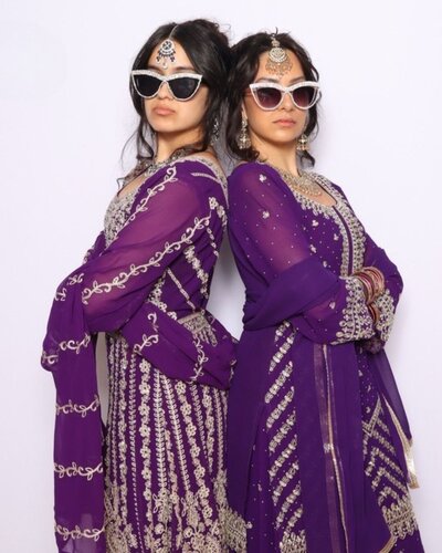 Two women in matching purple embroidered dresses and sunglasses posing back-to-back in front of a light backdrop at AR Photobooth.