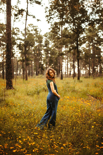 woman standing in field of wild flowers with trees in the background