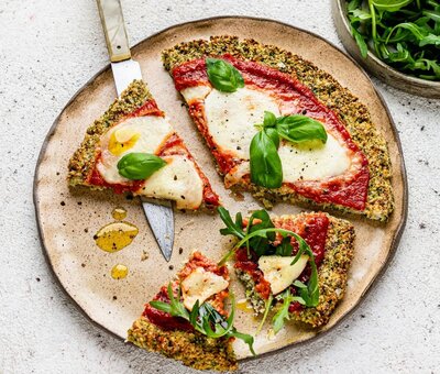 Gluten-free cauliflower crust pizza topped with tomato, mozzarella and fresh basil