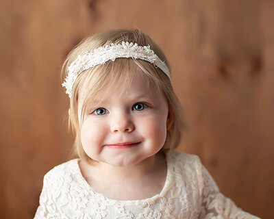 Toddler girl smiles for her first birthday pictures with headband .