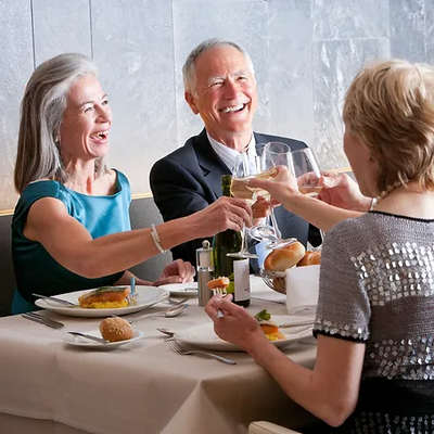 A group of older adults joyfully toasting with drinks at a dining table, celebrating a special occasion together.