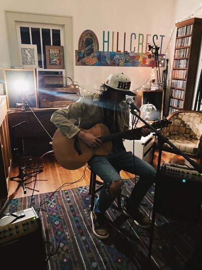 Man sits with guitar and sings into microphone at Hillcrest Coffee