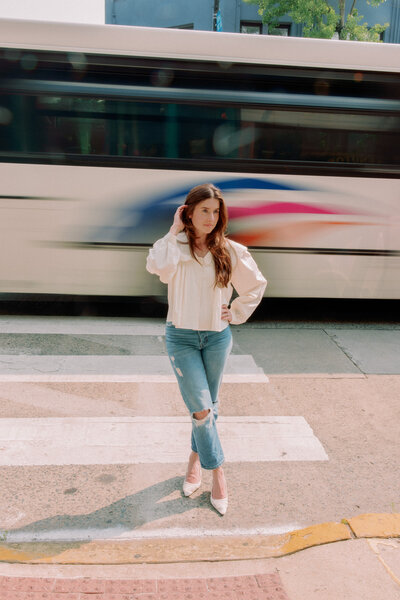 A person poses with their legs crossed and a hand in their hair while a bus goes by.