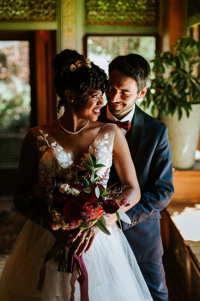A wedding couple embracing and smiling inside surrounded by plants in Detroit Michigan