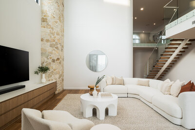 The Marisol home's living room, featuring a floor-to-ceiling stone feature wall, plush curved seating, and natural light-filled interiors.