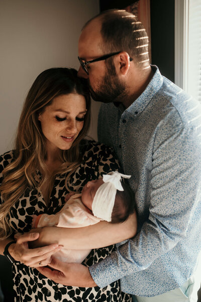 Woman holding her newborn baby and man kissing her head
