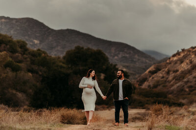 Expecting parents holding hands in a golden field near Corona, California during a maternity photo session