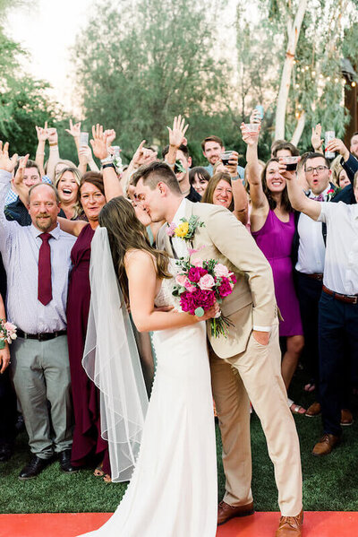 Bride and Groom Kissing with their family and friends cheering behind them