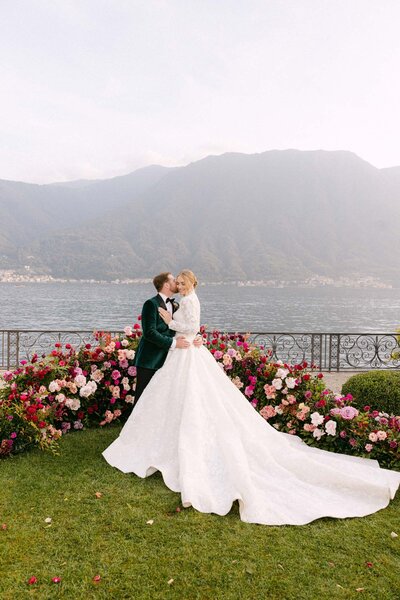 Bride and groom kissing with lavish florals and Lake Como in the background.