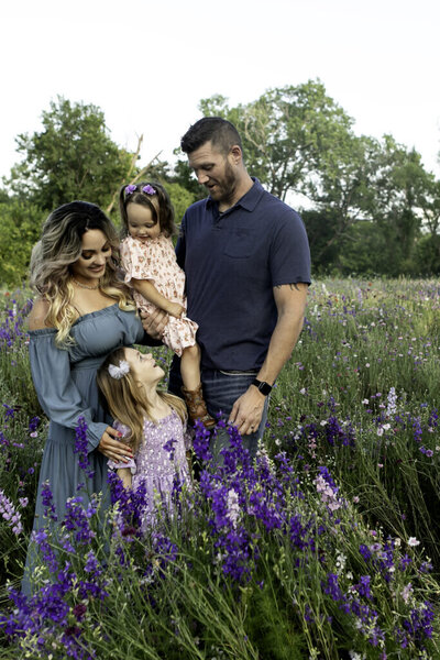 Happy family standing among the trees in Trinity Park, with natural greenery and sunlight filtering through the leaves during their photography shoot
