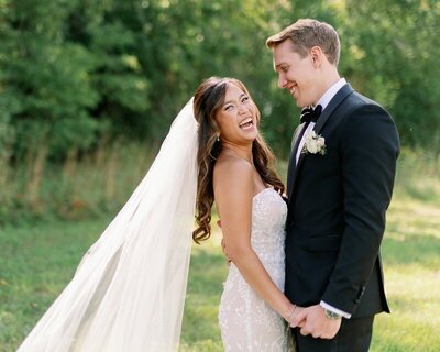 happy bride and groom outside on wedding day holding hands while bride grins to camera of bauer creative in minneapolis minnesota