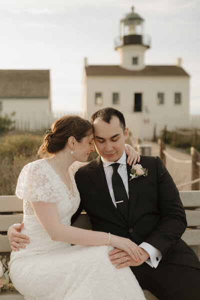 Couple cuddling on a bench outside of the Point Loma Lighthouse on their elopement day