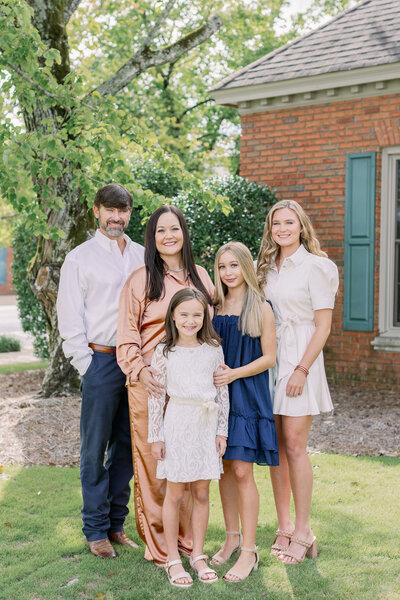 Family smiling in front of trees and a house