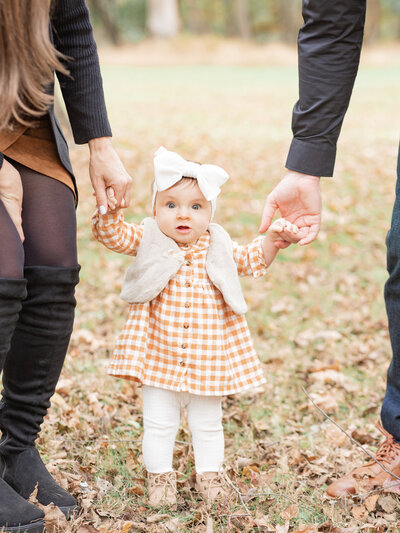 Allaire State Park baby girl in orange dress holding parents hands in fall