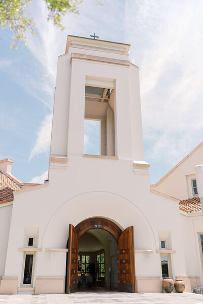 White, adobe-esque church with large wooden doors, and bell tower.
