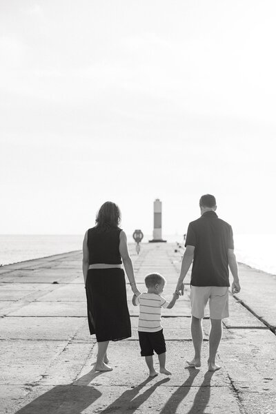 black and white portrait of a family on a pier walking toward a lighthouse