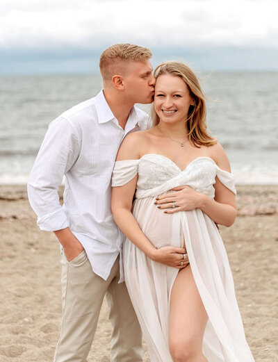 Romantic beach maternity session by Stamford CT photographer with couple in flowing white dress and linen shirt at waterfront location
