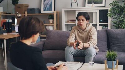 Teen boy sitting on couch speaking to a therapist