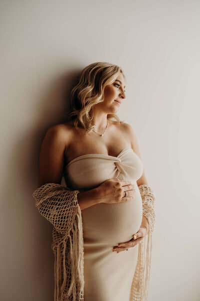 A young blonde soon to be mother looks off her left shoulder thoughtfully while she cradles her pregnant belly. during a photo session at free spirit photography.