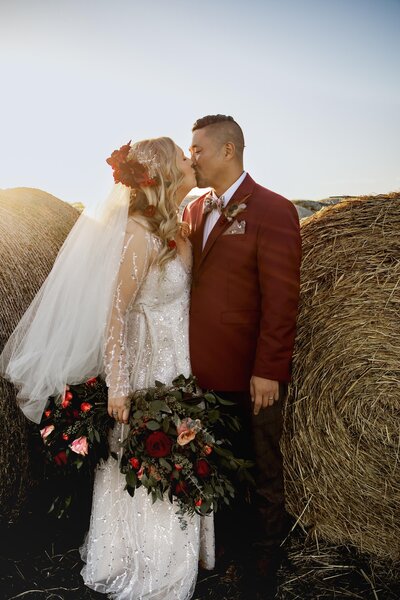 A bride and groom embrace in a kiss near the hay bales at a ranch in Prosper Texas