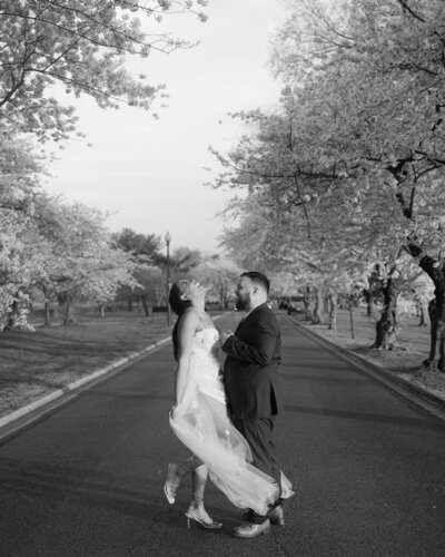 Couple posing for their engagement photos walking down a street with cherry blossoms lining the street.
