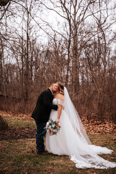 Bride and groom sharing a kiss in a wooded setting with fallen leaves
