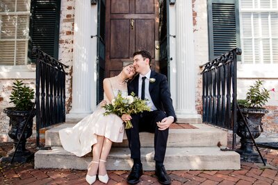 Two newlyweds sit on their doorstep with a bouquet in their lap