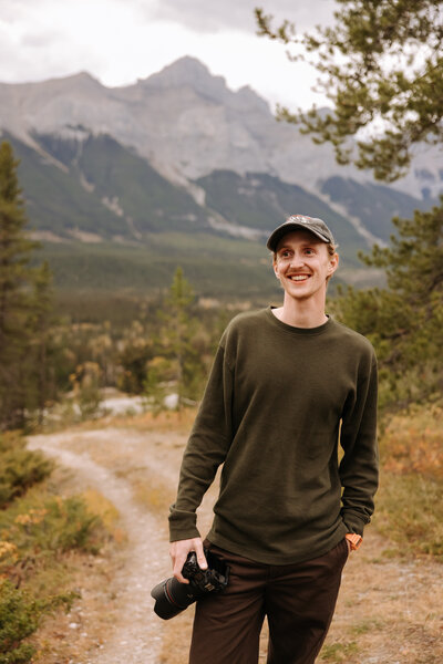 Event planner in cozy winter outfit and grey beanie smiling in snowy Banff forest – Rocky Mountain Wedding Collective