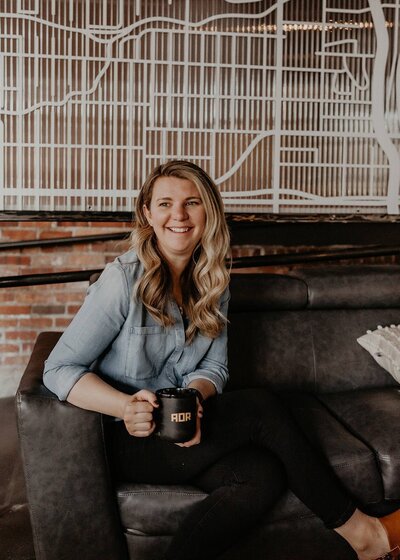 A woman sitting on a couch, holding a coffee mug, with a warm smile, representing her testimonial for Your True North.