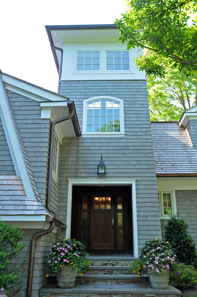 Shingle-style home entry in Sands Point featuring cedar siding, arched window, and wood front door.