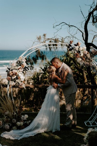 Modern boho luxe wedding flowers on a circular arbour overlooking the seaside venue of Sunshine Beach Surf Club, one of the most beautiful settings for a Sunshine Coast wedding.