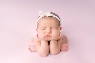 A newborn baby girl is posed with her hands under her chin.