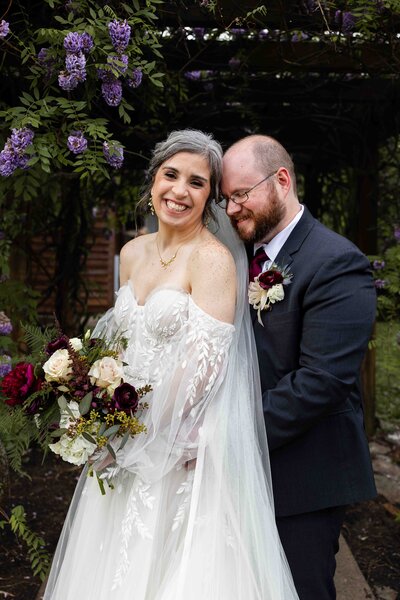 bride looking at camera smiling while groom nuzzles her temple