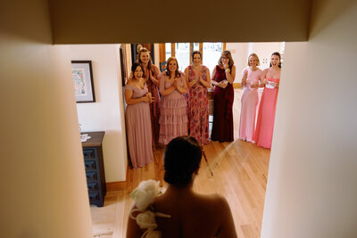bride coming down the stairs to her first look with her bridesmaids wearing pink floral dresses