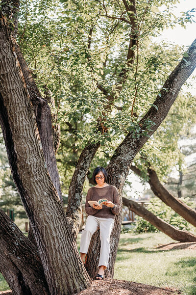 woman standing under a tree holding a book
