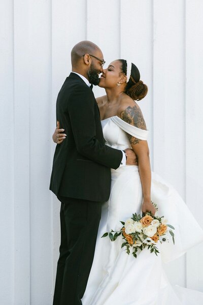 Bride and groom sharing a sweet kiss in front of a white wall