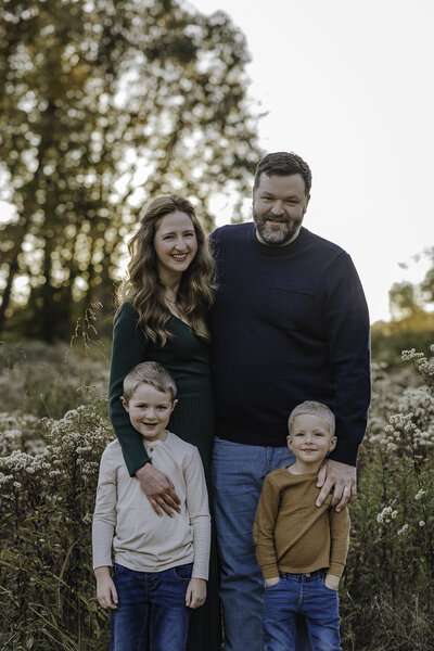 Verona B Photography captures a beautiful fall family photo of a mom, dad, and their two boys at Kendall Hills in Peninsula, OH. The family has their arms around each other and they are smiling at the camera. The fall colors were really at peak color and the sun was perfect for this family photo session near Akron.