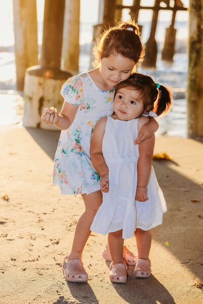 Two young girls share a loving moment on Cocoa Beach, arms linked, celebrating family time by the ocean.