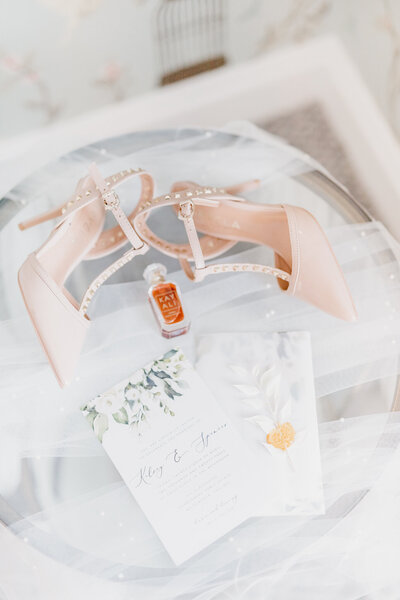 Bridal shoes, veil perfume and wedding invitation on a table during bridal preparations at Combermere Abbey in Cheshire