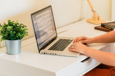 Branding photography with woman sitting at a white desk typing on her computer with plants next to her