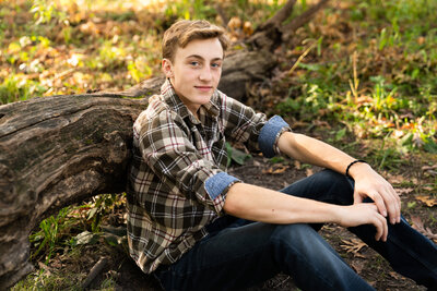 High school guy sits againts a log for his senior picture.