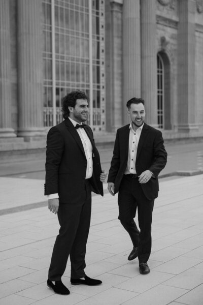 Two people in suits standing next to each other laughing 