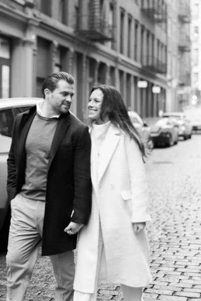 Couple smiles while holding hands as they walk through Soho NYC streets