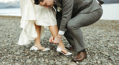 groom helping bride put on shoe during their wedding in Homer, Alaska.